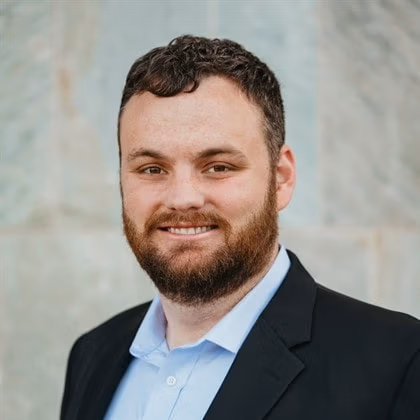 Ryan Sawyer, Chief Strategy Officer of Ethen Ostroff Law, smiling in a professional suit against a neutral backdrop, representing leadership and innovation in legal services.